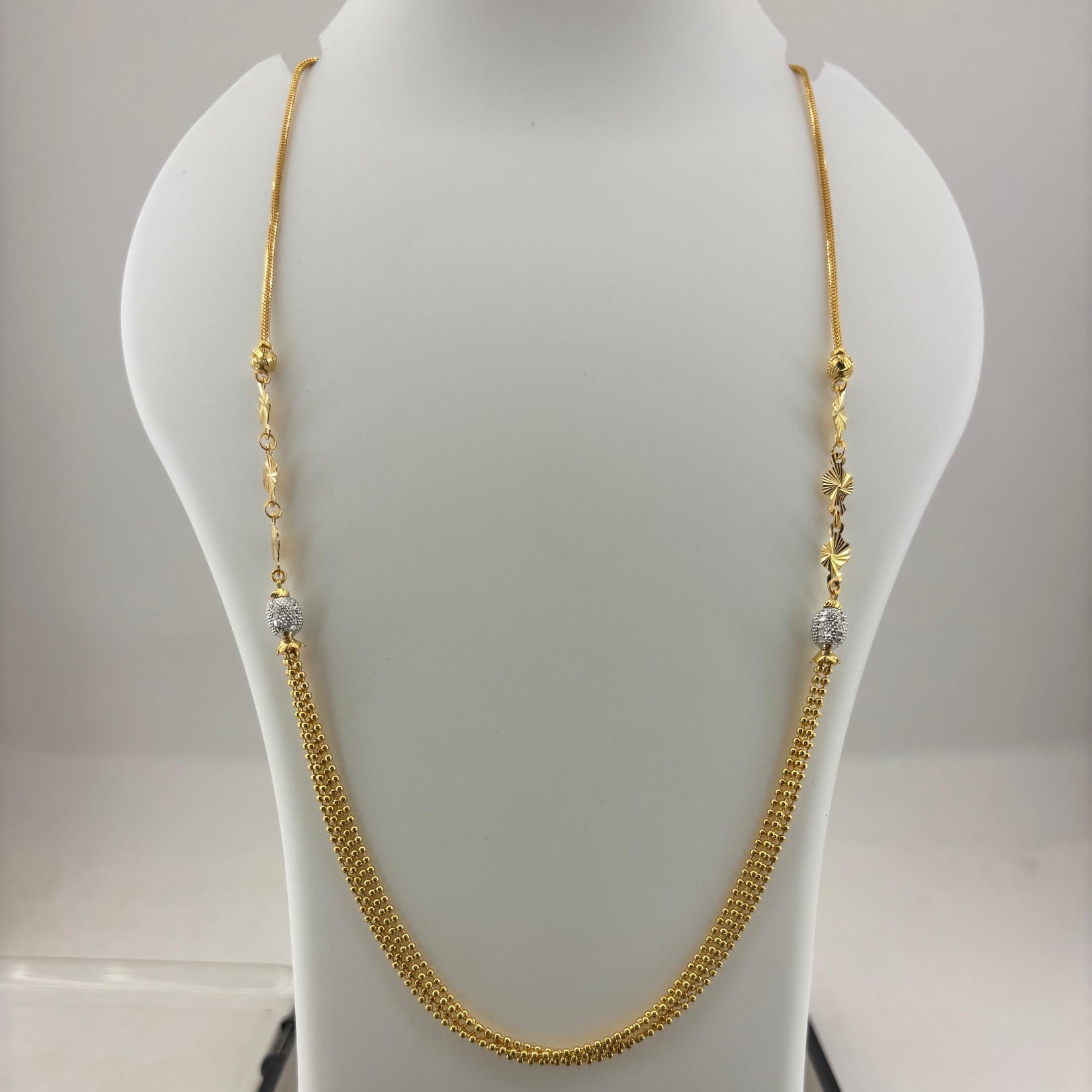 A gold chain necklace with small bead details and clear spacer beads, displayed on a white mannequin bust with a digital scale underneath.