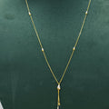 A delicate gold chain necklace with small bead accents and a teardrop-shaped pendant, displayed on a dark green velvet jewelry bust against a light gray background.