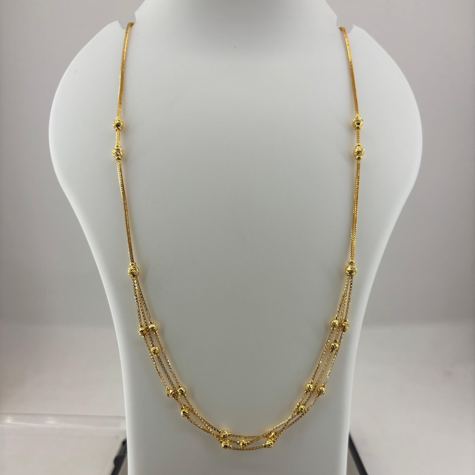 A gold multi-strand beaded necklace displayed on a white mannequin bust, with a digital scale visible underneath.
