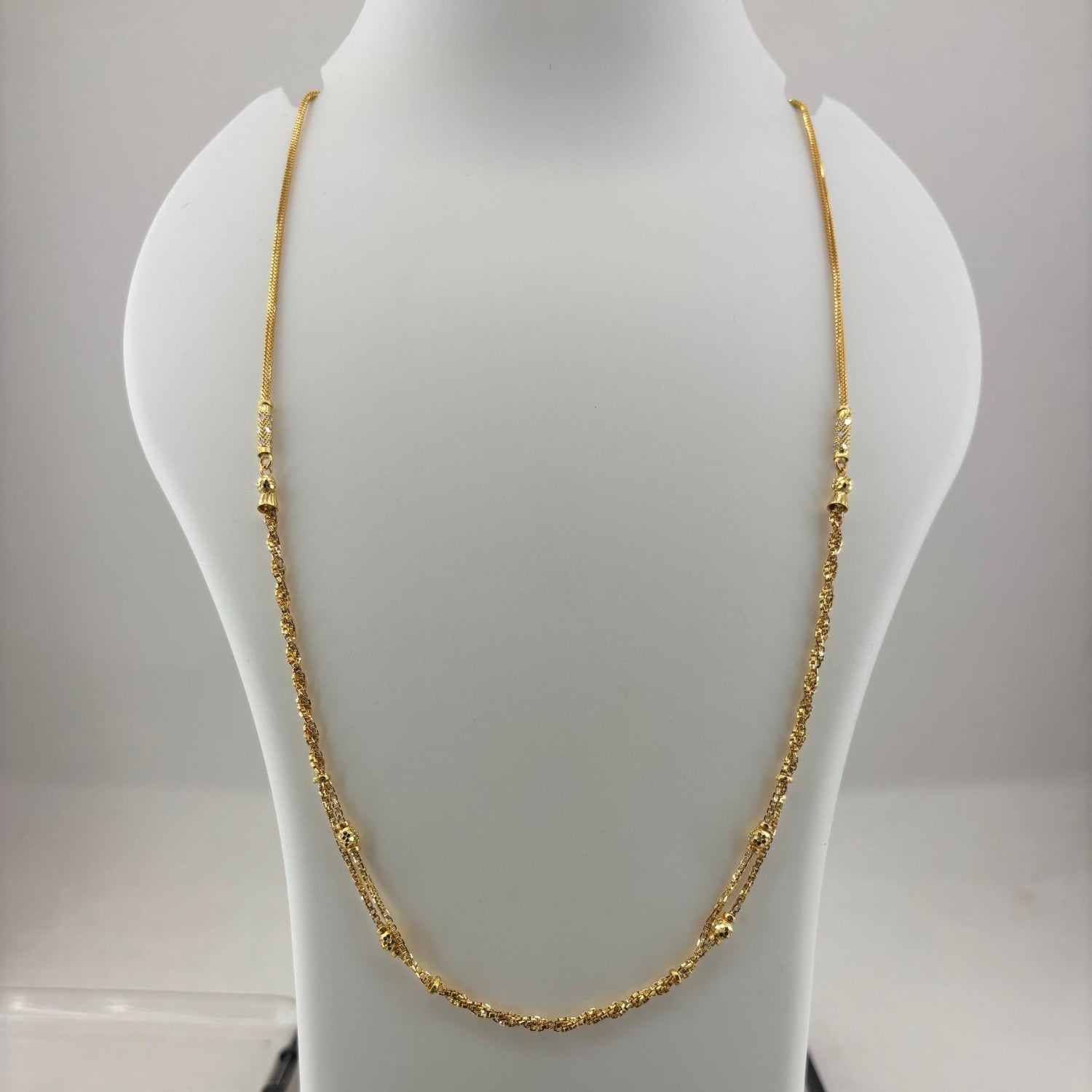 A gold chain necklace displayed on a white mannequin bust, with a digital scale visible underneath. The scale screen shows a weight reading of 8.