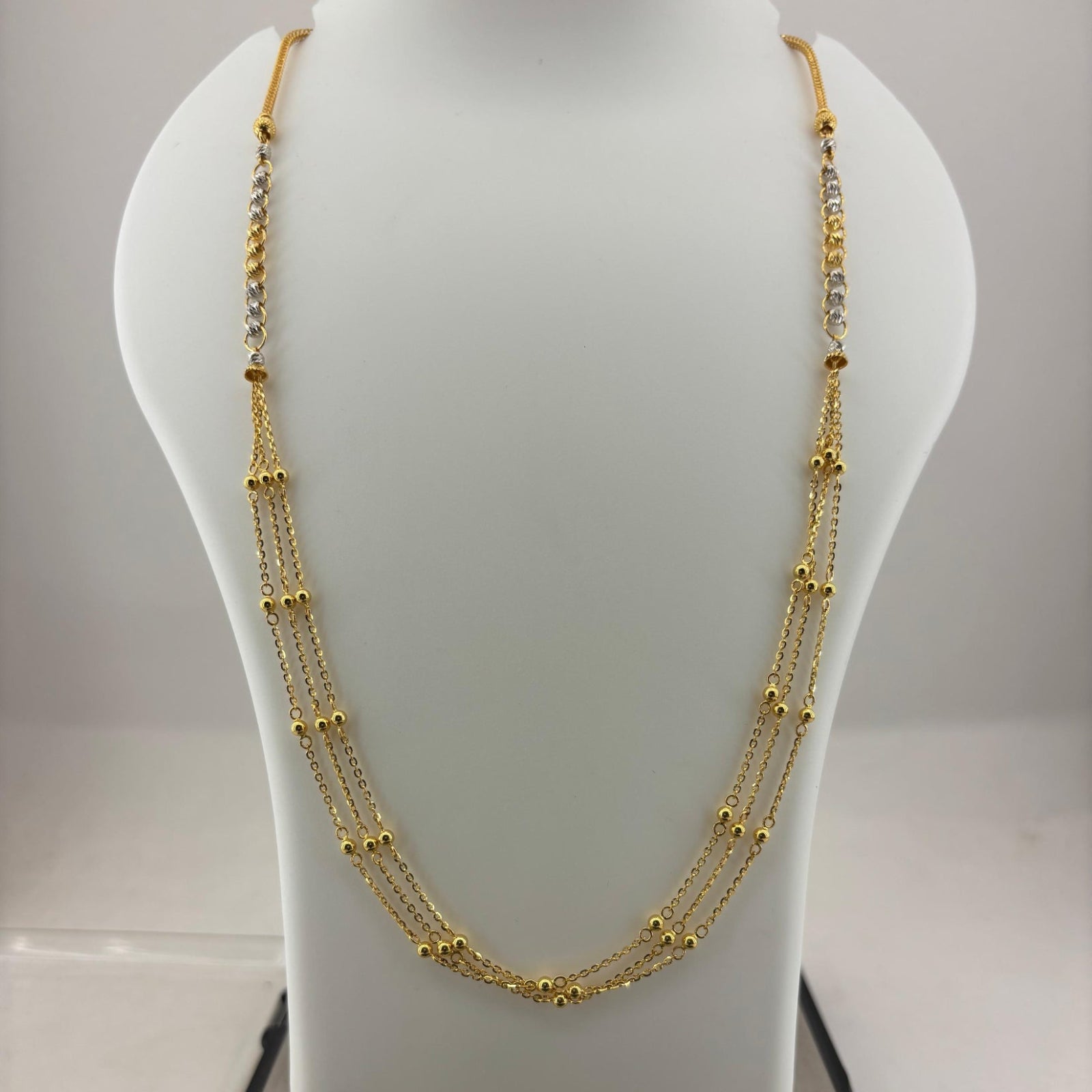 A multi-strand gold necklace displayed on a white mannequin bust, with a digital scale visible underneath to show the weight.