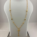 A gold necklace with a small floral pendant and dangling tassel, displayed on a white mannequin bust with a digital scale underneath.