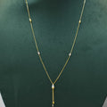 A delicate gold chain necklace with a teardrop-shaped clear stone pendant and small gold bead accents, displayed on a dark green jewelry bust.
