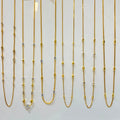 Six gold-toned chain necklaces with mixed metal bead and link details are displayed on a white jewelry stand, each with a small white price tag attached.