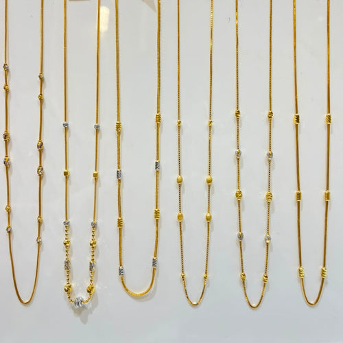 Six gold-toned chain necklaces with mixed metal bead and link details are displayed on a white jewelry stand, each with a small white price tag attached.