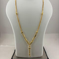 A gold necklace displayed on a white mannequin bust, with a digital scale visible underneath. The necklace features a delicate chain with small bead details and a central pendant with a vertical drop.