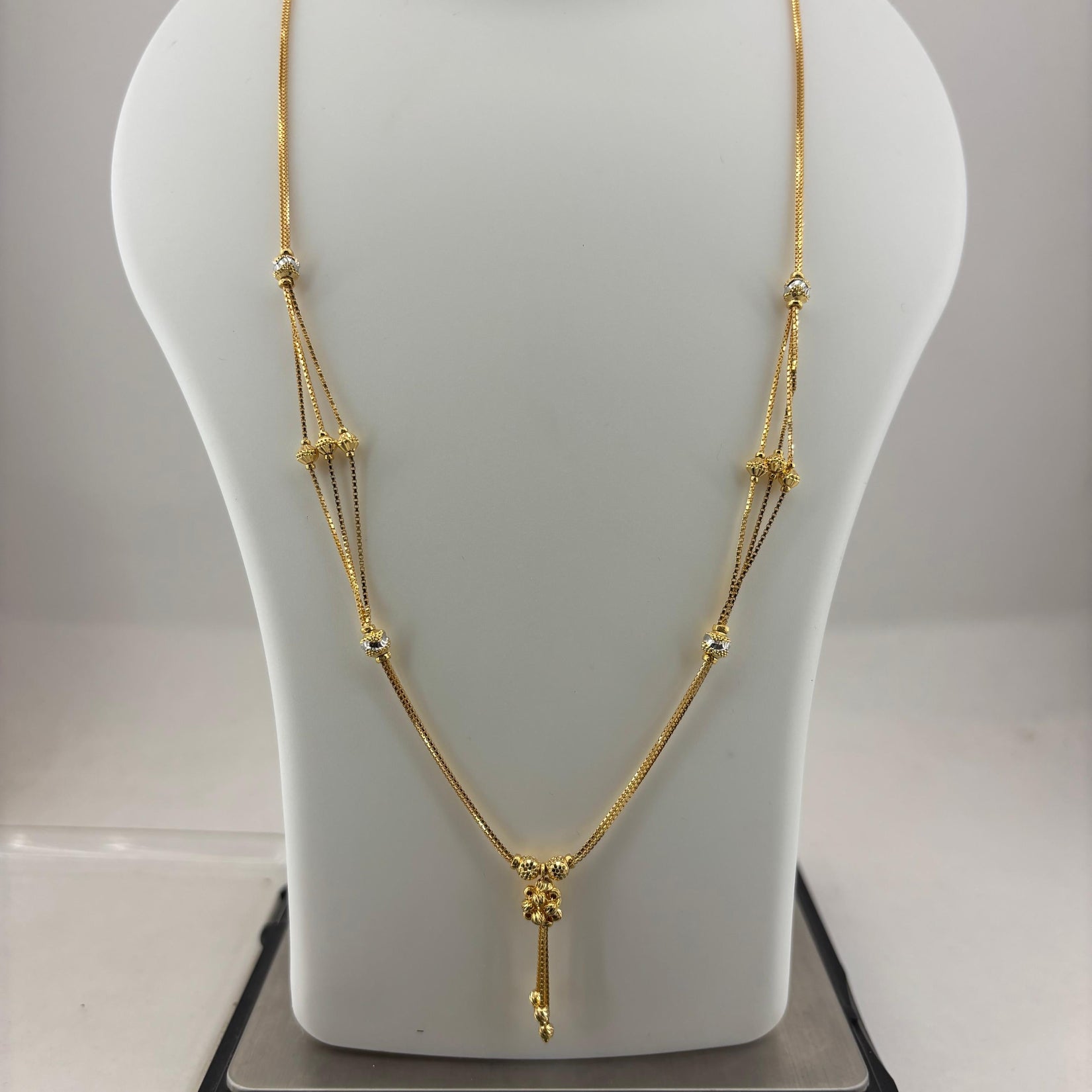 A gold-toned multi-strand necklace with a small pendant, displayed on a white mannequin bust sitting on a digital scale showing 8.54 grams.