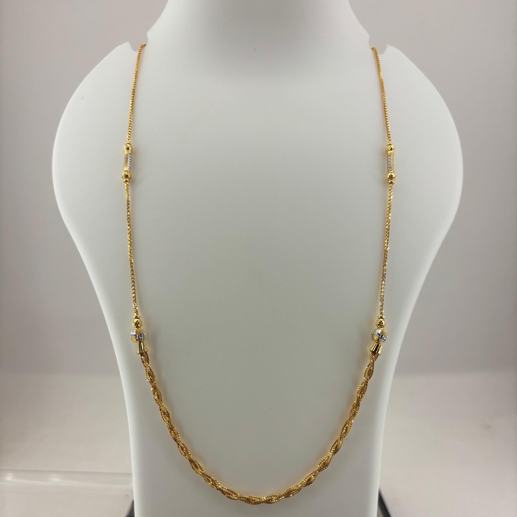 A gold chain necklace displayed on a white mannequin bust, with a digital scale visible underneath.