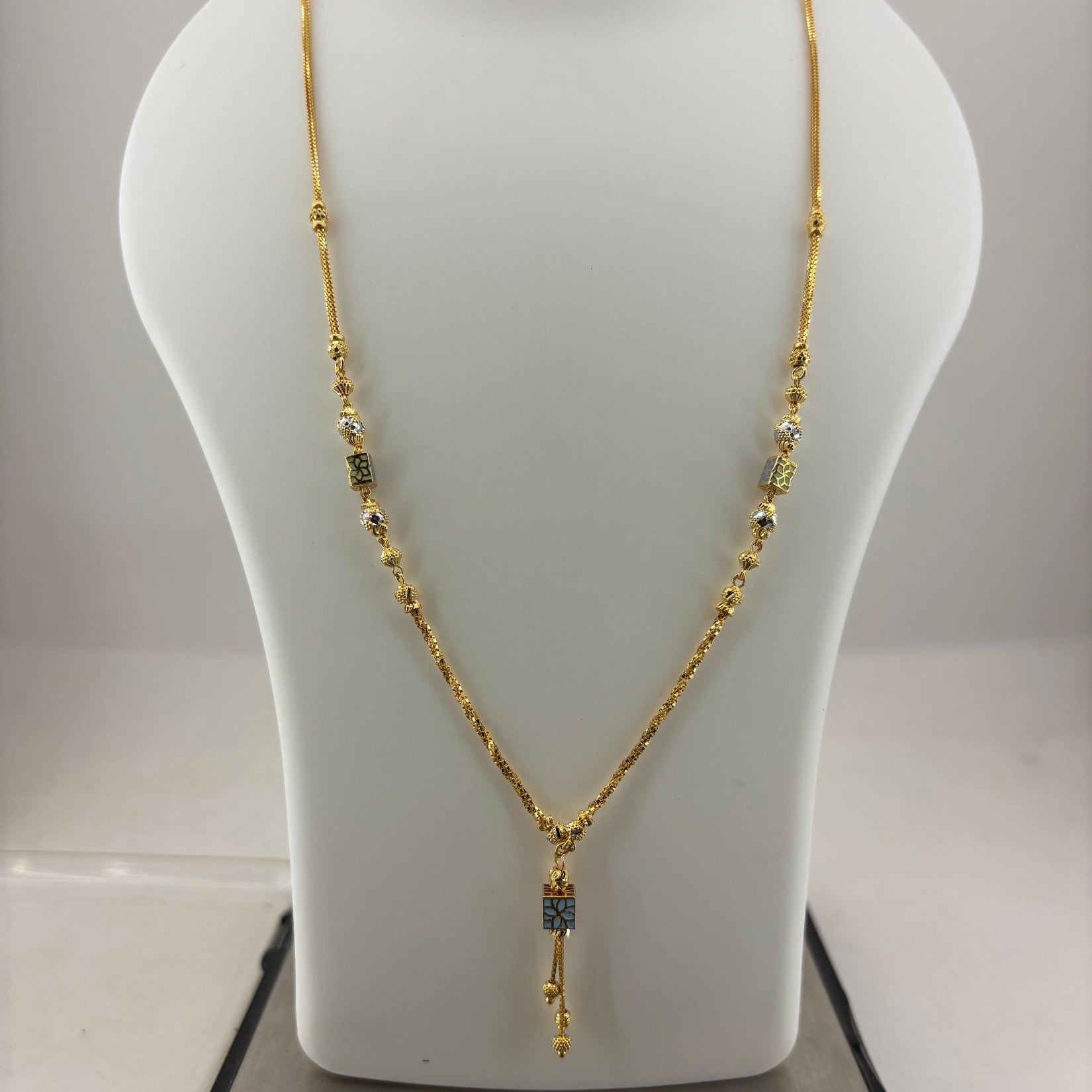 A gold necklace with small green bead accents and a dangling rectangular pendant, displayed on a white jewelry bust atop a digital scale showing 93.7 grams.