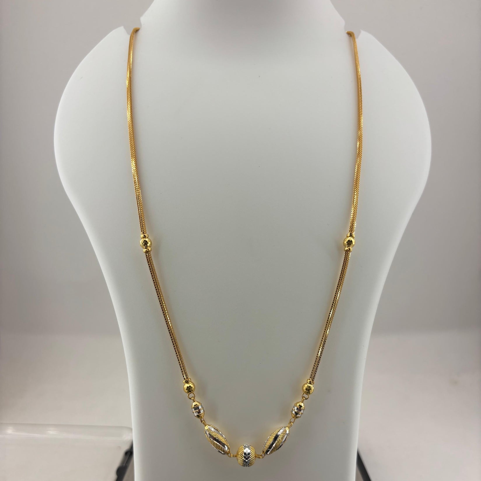 A gold chain necklace with small bead details and a central decorative pendant, displayed on a white jewelry bust over a digital scale showing 11.8 grams.