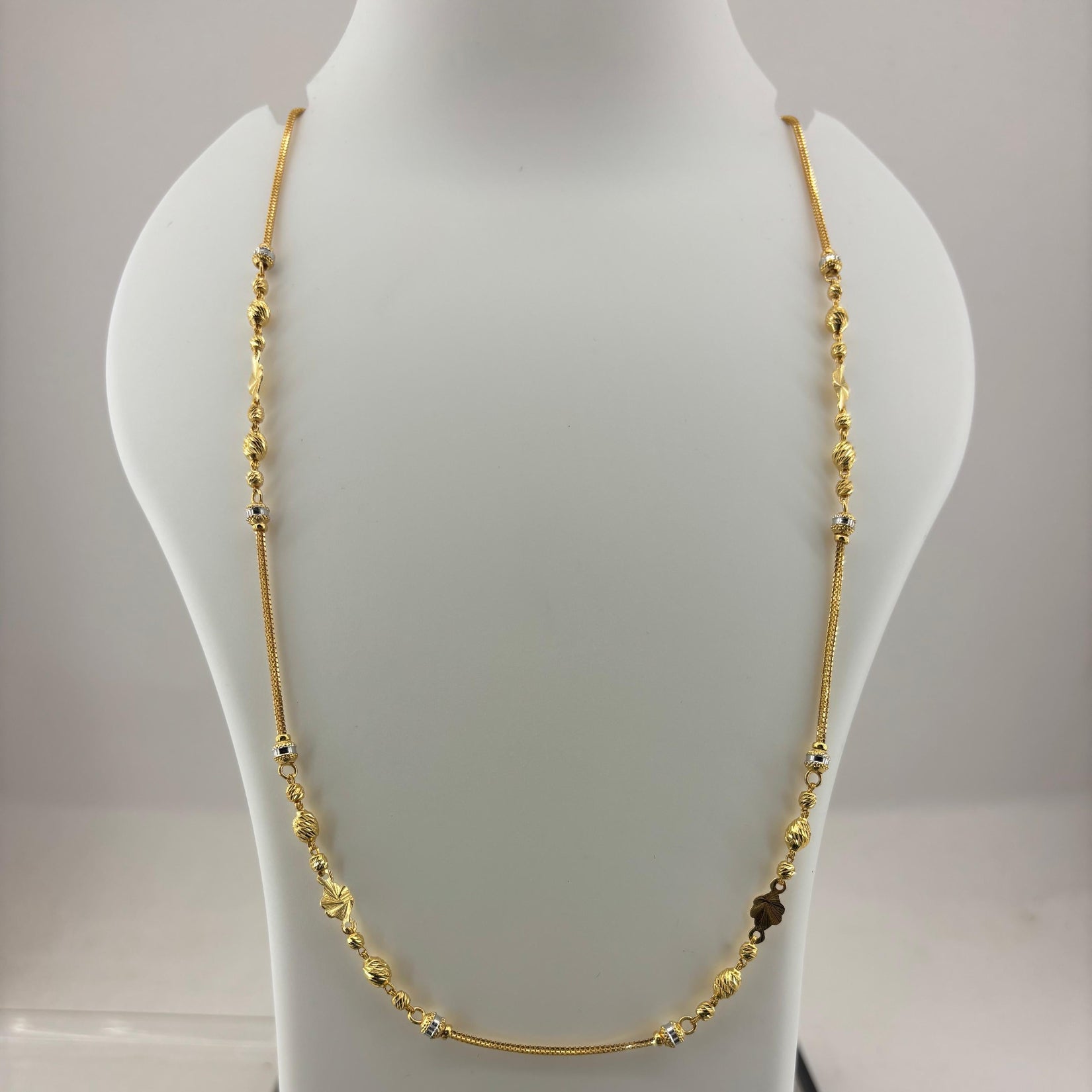 A gold-toned beaded necklace displayed on a white mannequin bust, with a digital scale visible underneath.