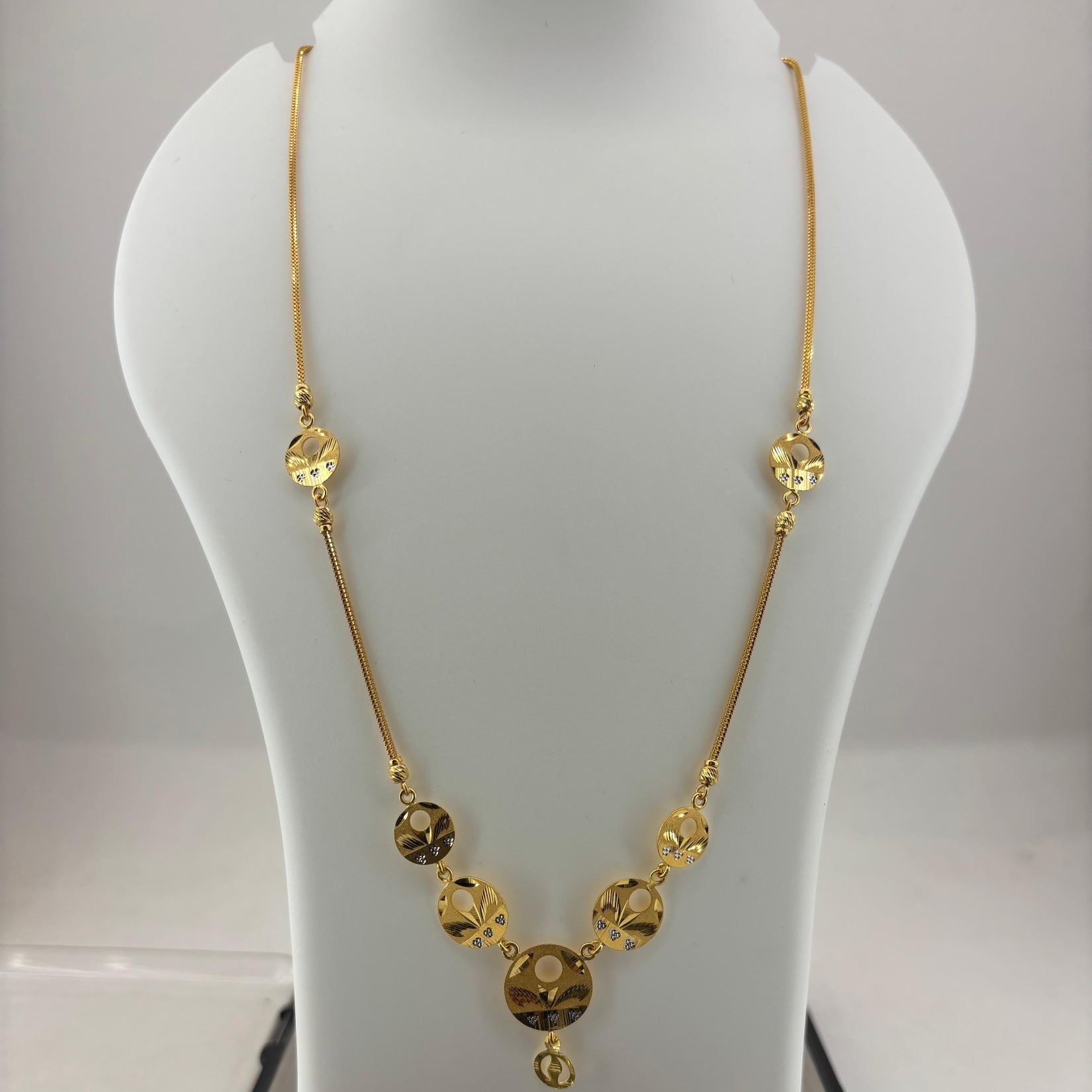 A gold chain necklace with faceted round beads and a central pendant, displayed on a white mannequin bust over a digital scale showing 8.75 grams.