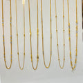 Nine gold chains of varying lengths and styles displayed on a white stand, each with a small price tag attached.