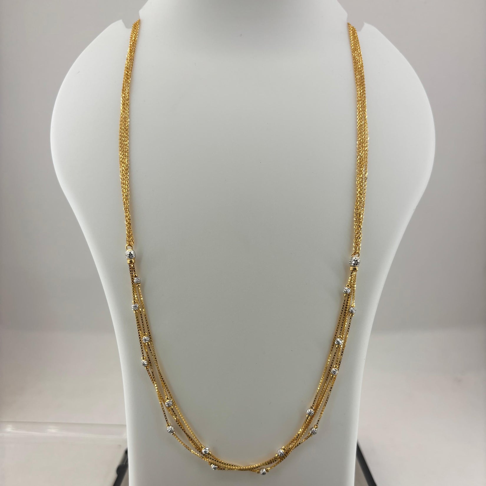 A gold-toned multi-strand necklace displayed on a white mannequin bust, with a digital scale visible underneath.
