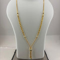 A gold necklace displayed on a white mannequin bust, with a digital scale visible underneath. The necklace features a twisted rope chain, small bead details, and a central pendant with hanging tassels.