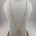 A gold necklace displayed on a white mannequin bust, with a digital scale visible underneath. The necklace features a delicate chain with small bead-like accents and a central pendant with three dangling chain ends.
