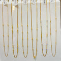 Nine gold beaded chains of varying lengths displayed on a white stand, each with a small white price tag attached.