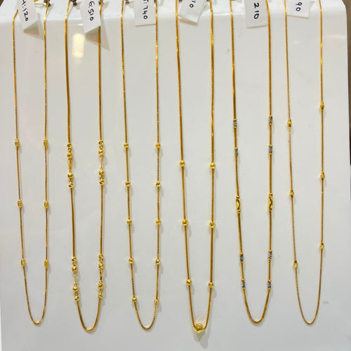 Nine gold beaded chains of varying lengths displayed on a white stand, each with a small white price tag attached.