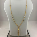 A gold chain necklace with small clear beads and a dangling gold tassel pendant, displayed on a white mannequin bust resting on a digital scale.