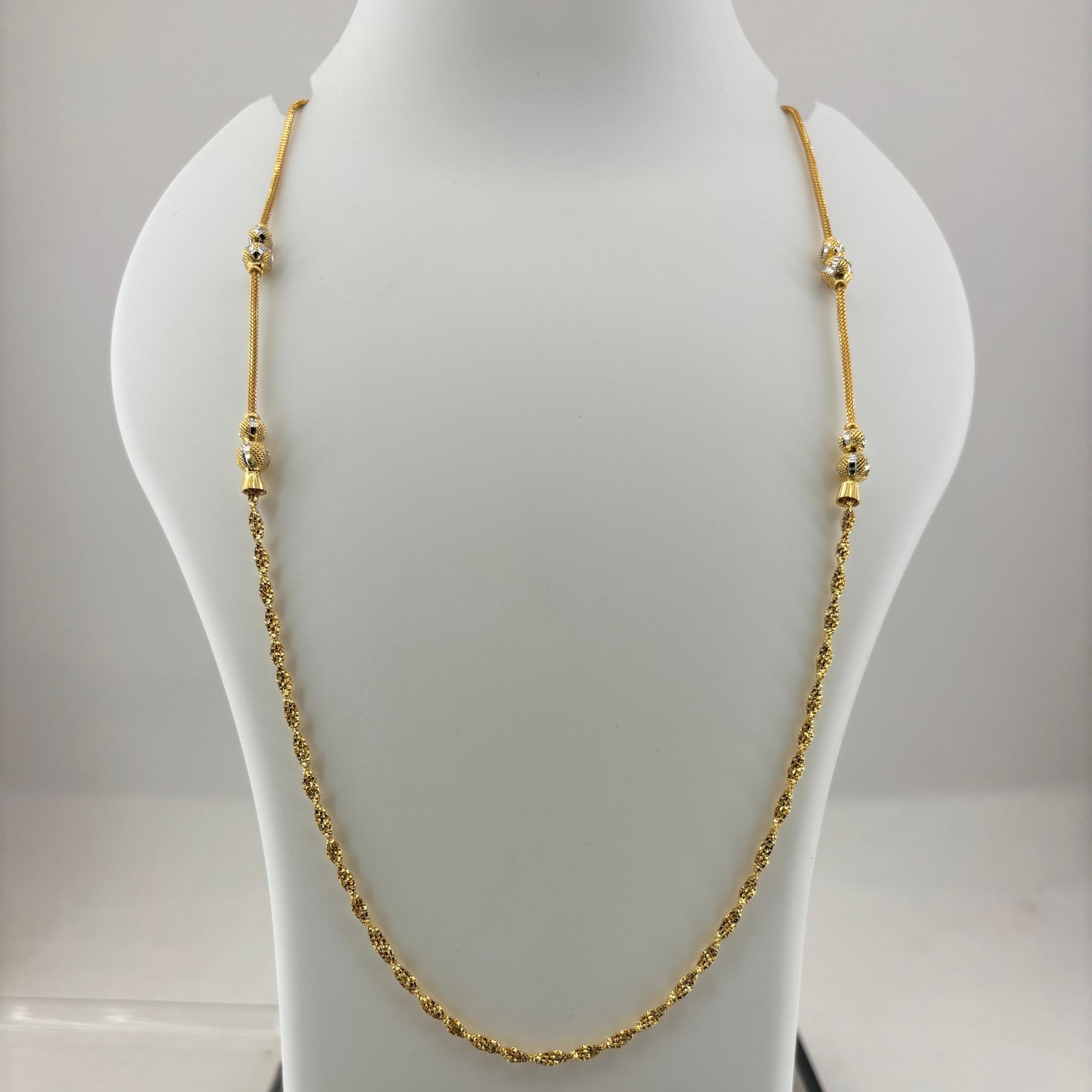 A gold chain necklace with small bead-like links and decorative spacer beads, displayed on a white jewelry bust. The bust is placed on top of a digital scale showing a weight of 8.