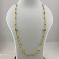 A gold necklace with small bead-like links and a central crisscross design, displayed on a white jewelry bust above a digital scale.