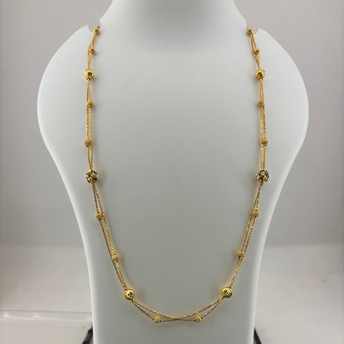 A gold necklace with small bead-like links and a central crisscross design, displayed on a white jewelry bust above a digital scale.