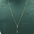 A delicate gold necklace with small bead details and a teardrop-shaped pendant, displayed on a dark green jewelry bust.
