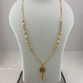 A gold necklace with a key-shaped pendant displayed on a white mannequin bust, with a digital scale visible underneath.