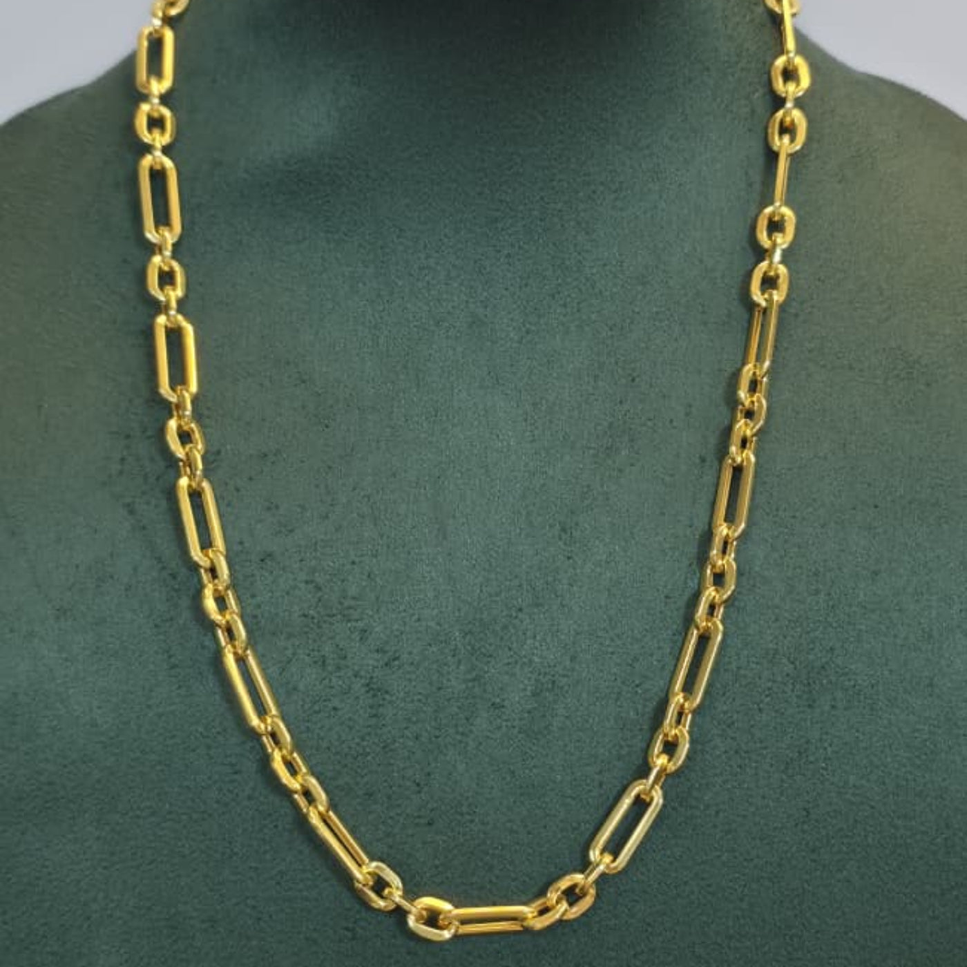 A gold chain necklace with elongated oval links displayed on a dark green jewelry bust against a light gray background.