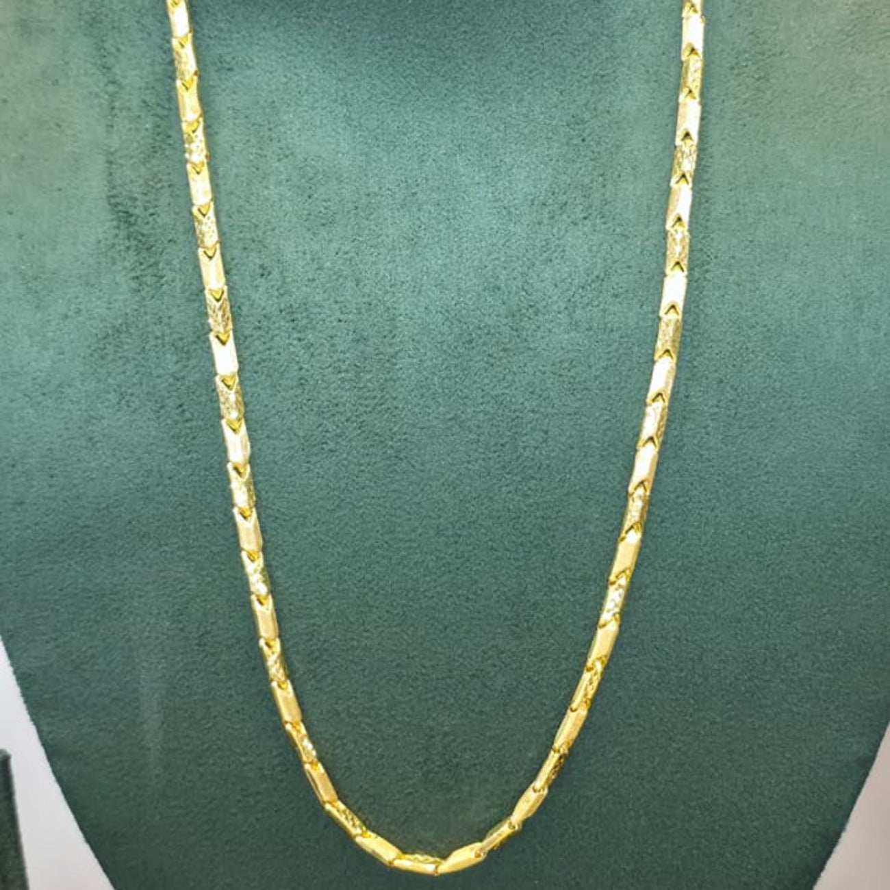 A gold chain necklace displayed on a dark green velvet jewelry bust against a plain light background.