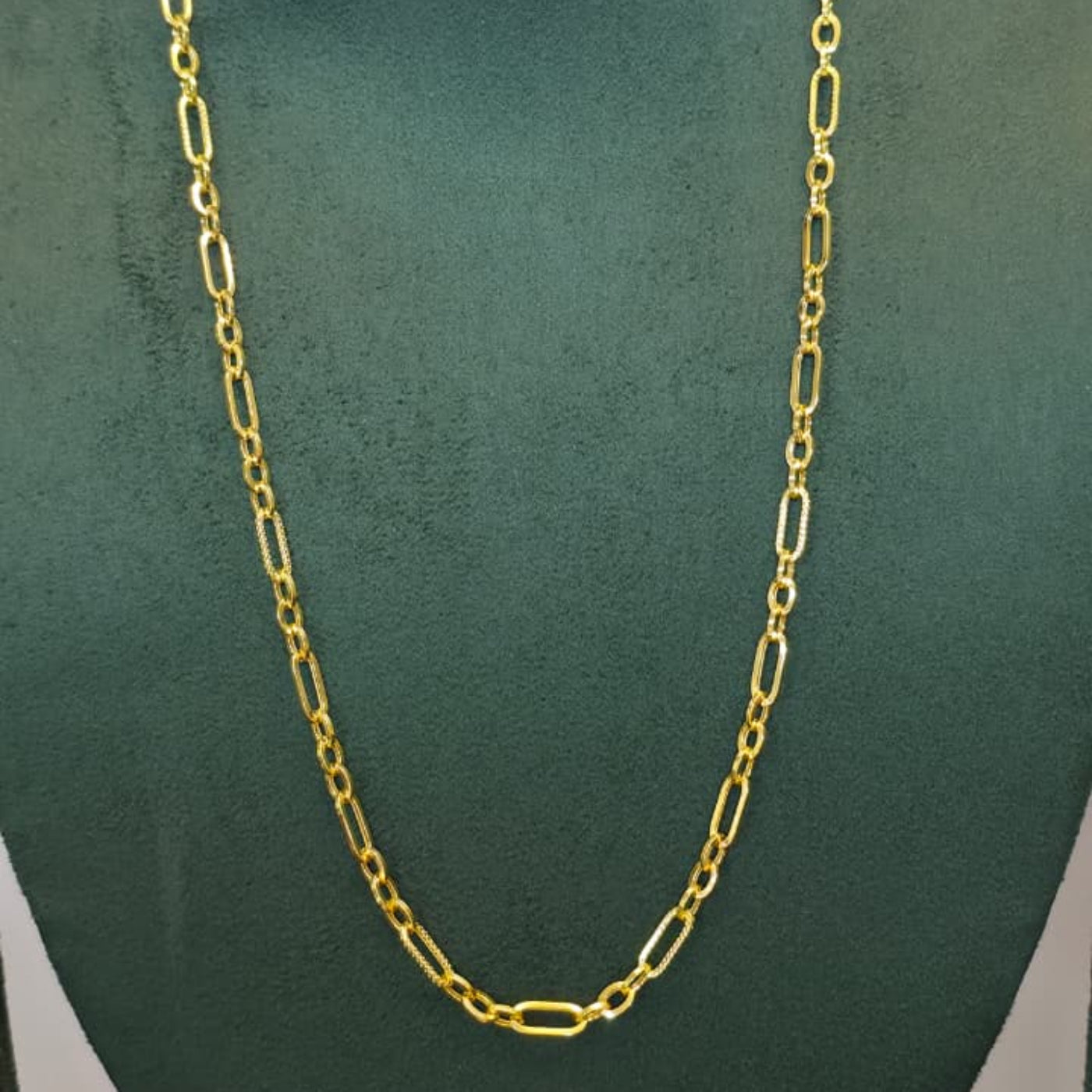 A gold paperclip chain necklace displayed on a dark green velvet jewelry bust against a light gray background.