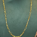 A gold-colored Figaro chain necklace displayed on a dark green velvet jewelry bust.