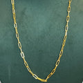 A gold paperclip chain necklace displayed on a dark green velvet jewelry bust against a light gray background.
