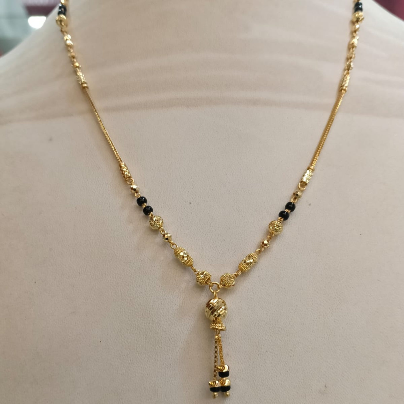 Gold necklace with small black bead accents and a dangling pendant, displayed on a beige mannequin bust.