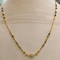 A gold chain necklace with small black bead accents and a central silver-toned pavé stone, displayed on a beige jewelry bust.