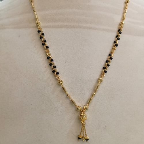 Gold necklace with black bead accents and a small dangling tassel charm, displayed on a cream-colored mannequin bust.