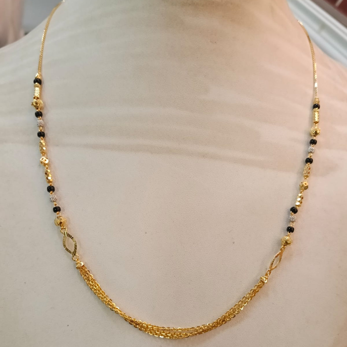 A gold chain necklace with small black and gold beads, displayed on a cream-colored mannequin bust.