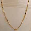 A gold chain necklace with small black beads and decorative gold spacer elements, displayed on a cream-colored mannequin bust.