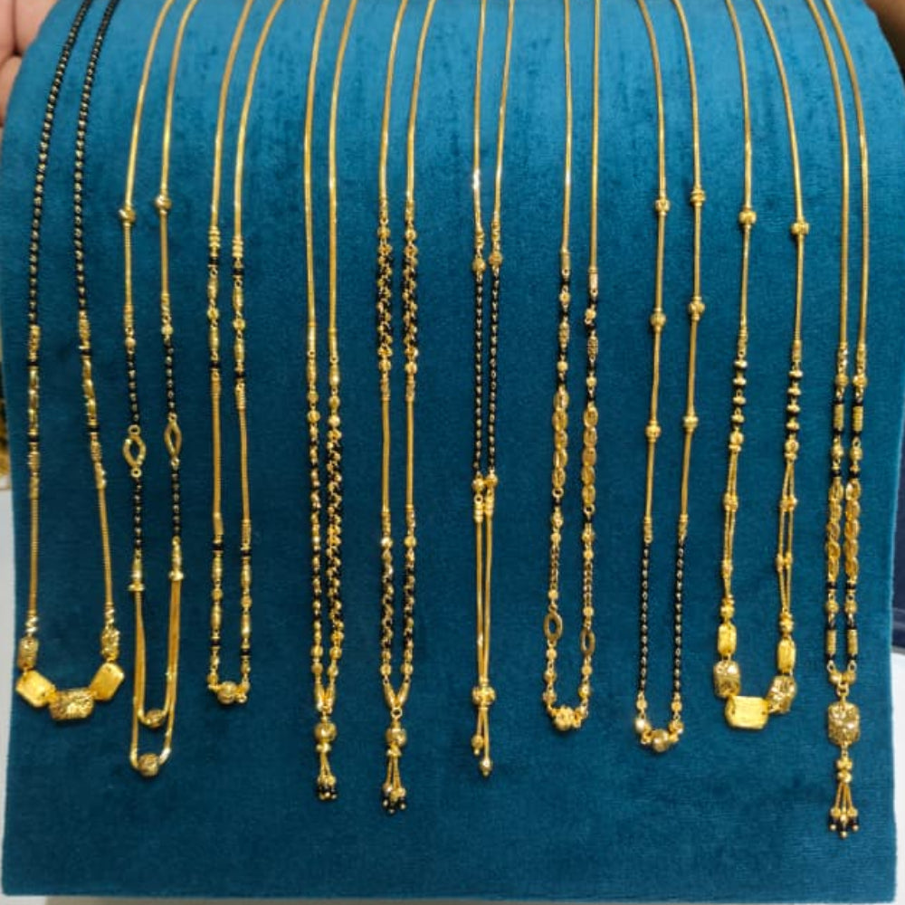 A display of multiple gold necklaces with various bead and pendant designs, arranged on a teal velvet jewelry stand. A hand is visible on the left holding the stand, and a person in a blue striped shirt is partially visible on the right.