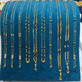 A display of multiple gold-toned beaded necklaces and chains arranged on a teal velvet jewelry stand, photographed on a white tabletop with a person partially visible in the background.