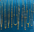A hand holds up a teal velvet jewelry display bust filled with multiple gold-tone and black beaded necklaces, shown against a retail counter with papers and a phone in the background.