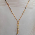 A gold-toned beaded necklace with black and white beads, displayed on a white mannequin bust.