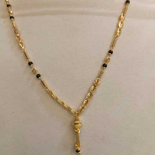 A gold chain necklace with small black bead accents, displayed on a cream-colored mannequin bust.